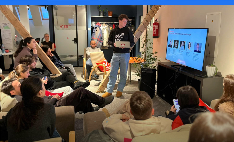 A person standing in front of a group of people sitting on couches
Description automatically generated