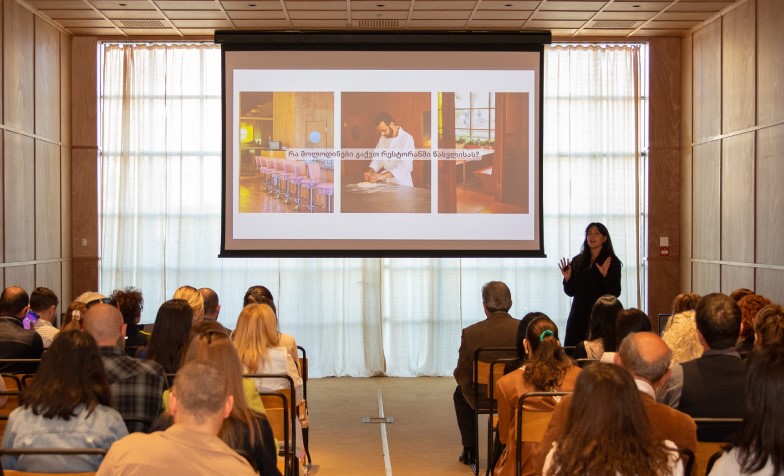 A person standing in front of a projection screen 
Description automatically generated